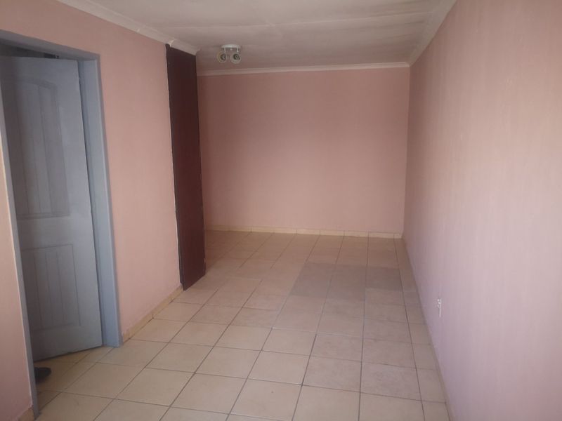 An empty, neutrally painted living area featuring tiled flooring and a ceiling-mounted spotlight fixture.