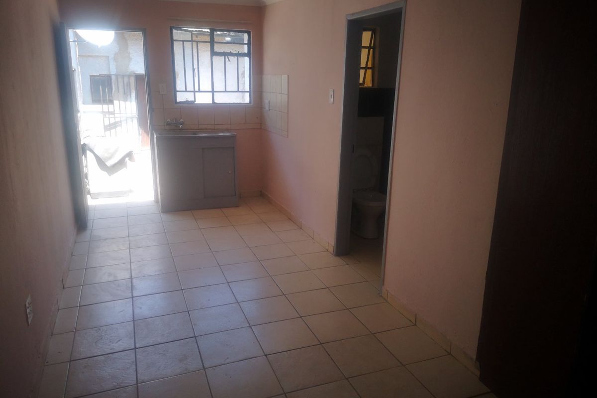 A basic, empty kitchen area featuring tiled flooring, a sink, and a doorway leading to an adjacent bathroom.