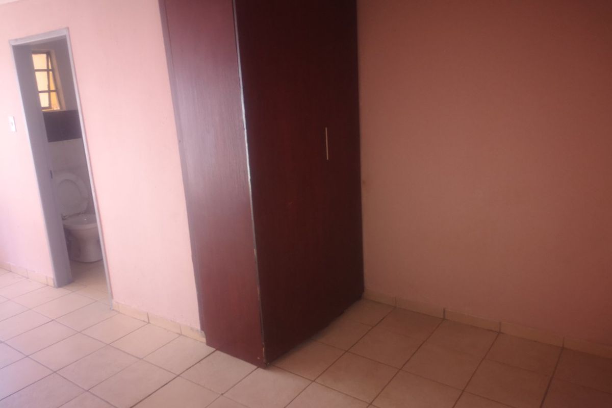 An empty bedroom featuring tiled flooring and a built-in wardrobe, with an adjacent view into a bathroom area.
