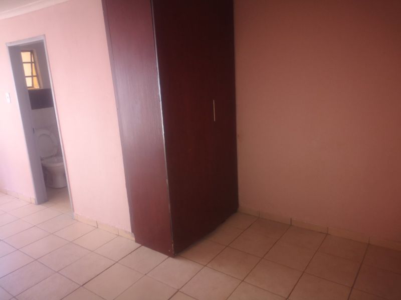 An empty bedroom featuring tiled flooring and a built-in wardrobe, with an adjacent view into a bathroom area.