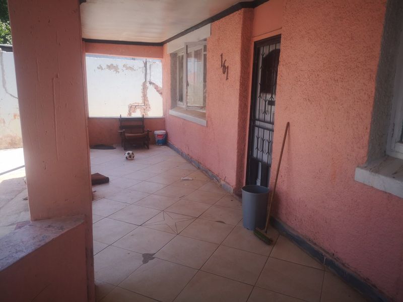 A covered front patio area featuring tiled flooring, a security gate, and textured exterior walls in need of maintenance and cosmetic updates.