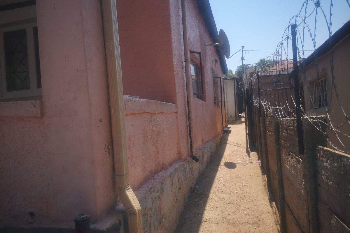 Side passage of the property featuring a precast concrete wall with razor wire security fencing and weathered exterior wall finishes.