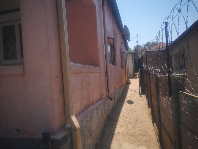 Side passage of the property featuring a precast concrete wall with razor wire security fencing and weathered exterior wall finishes.