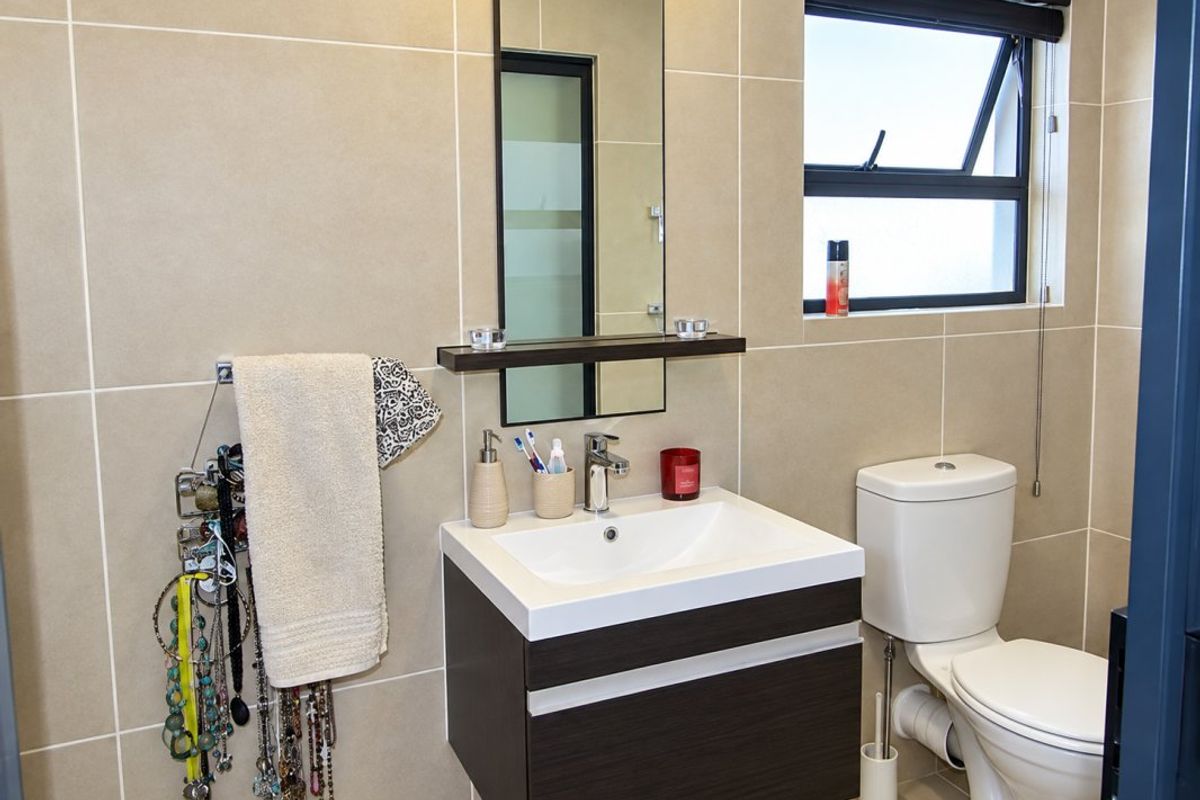 A modern bathroom featuring a wall-mounted vanity with a ceramic basin, a sleek mirror, and neutral wall tiling.