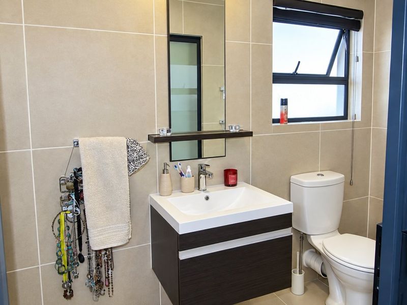 A modern bathroom featuring a wall-mounted vanity with a ceramic basin, a sleek mirror, and neutral wall tiling.