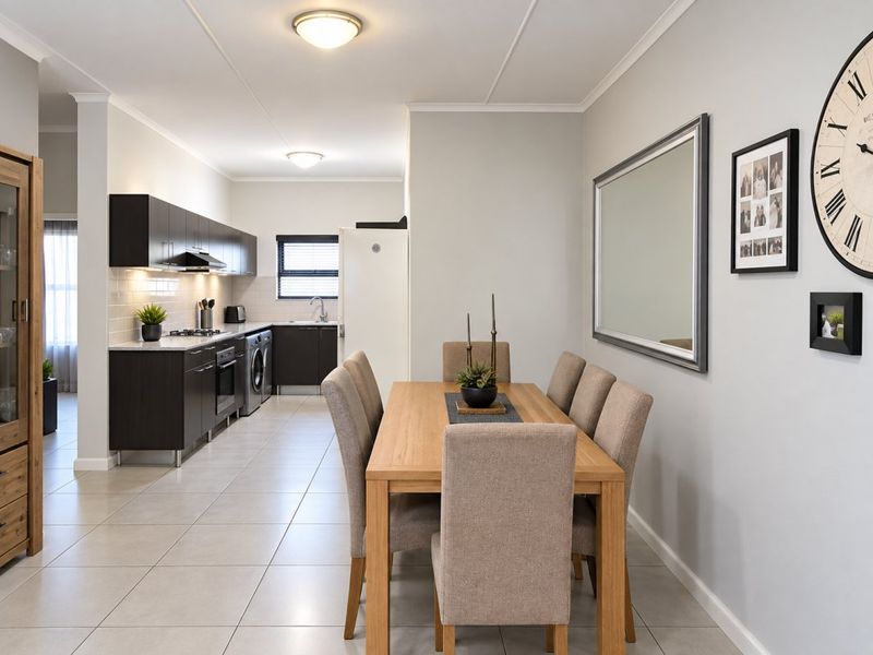 Open-plan kitchen and dining area featuring modern dark cabinetry, tiled flooring, and integrated appliances, creating a functional and cohesive living space.