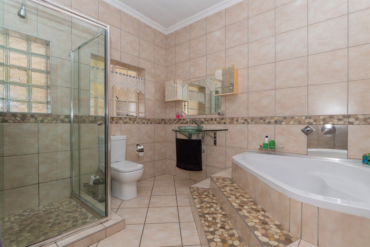 A spacious bathroom featuring a glass shower enclosure, a raised built-in bathtub with decorative tiling, and a wall-mounted glass basin.