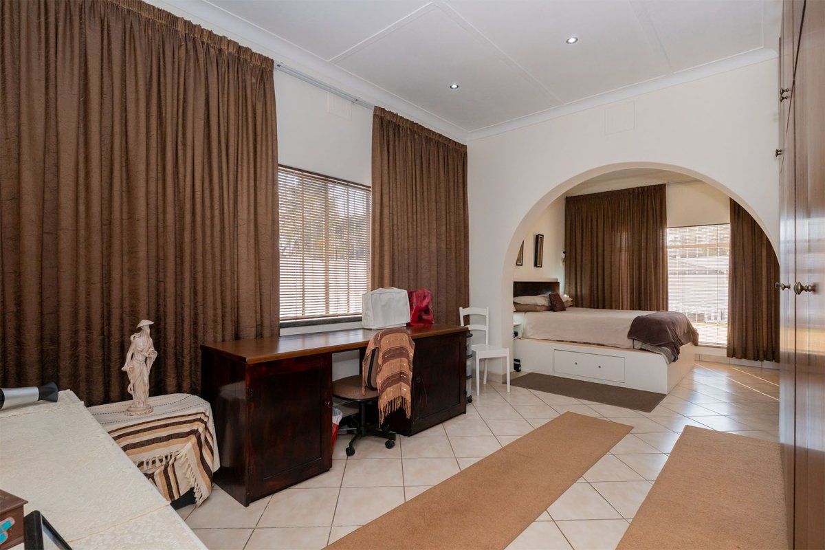 Spacious bedroom featuring tiled flooring, recessed downlighting, and a distinctive architectural archway leading to the sleeping area with built-in storage.