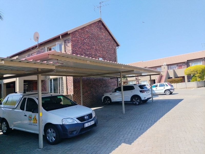 Exterior view of an apartment complex featuring a covered carport area with paved driveway and brick building facade.