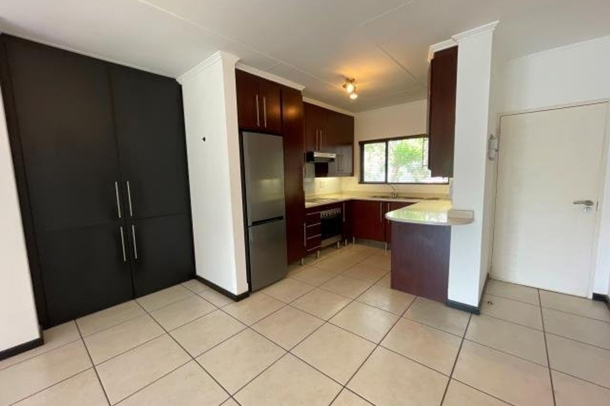 A functional kitchen featuring dark wood cabinetry, built-in oven, extractor fan, and a breakfast counter with tiled flooring throughout.
