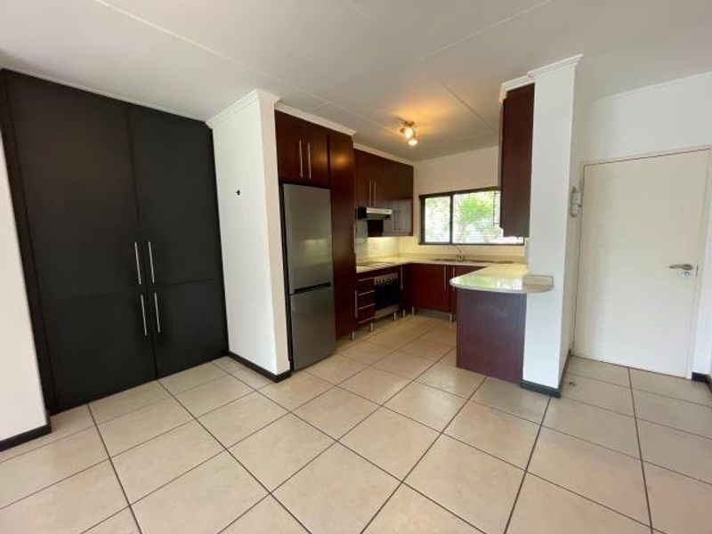 A functional kitchen featuring dark wood cabinetry, built-in oven, extractor fan, and a breakfast counter with tiled flooring throughout.