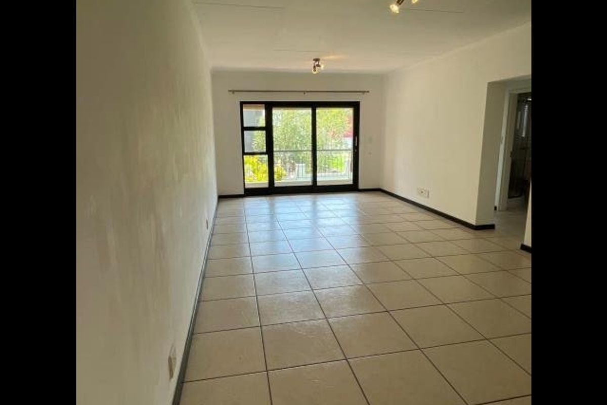 An empty, open-plan living area featuring neutral tiled flooring and a large sliding glass door providing access to an outdoor space.