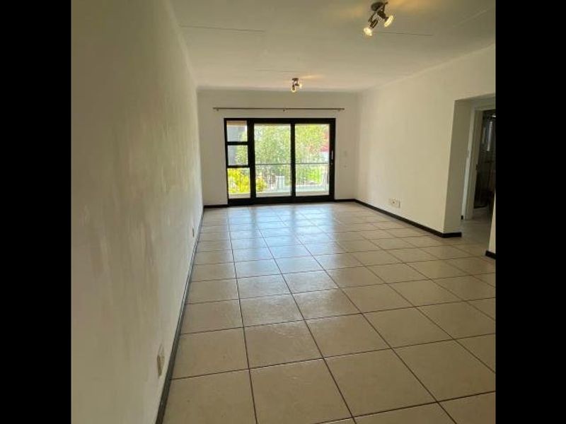 An empty, open-plan living area featuring neutral tiled flooring and a large sliding glass door providing access to an outdoor space.