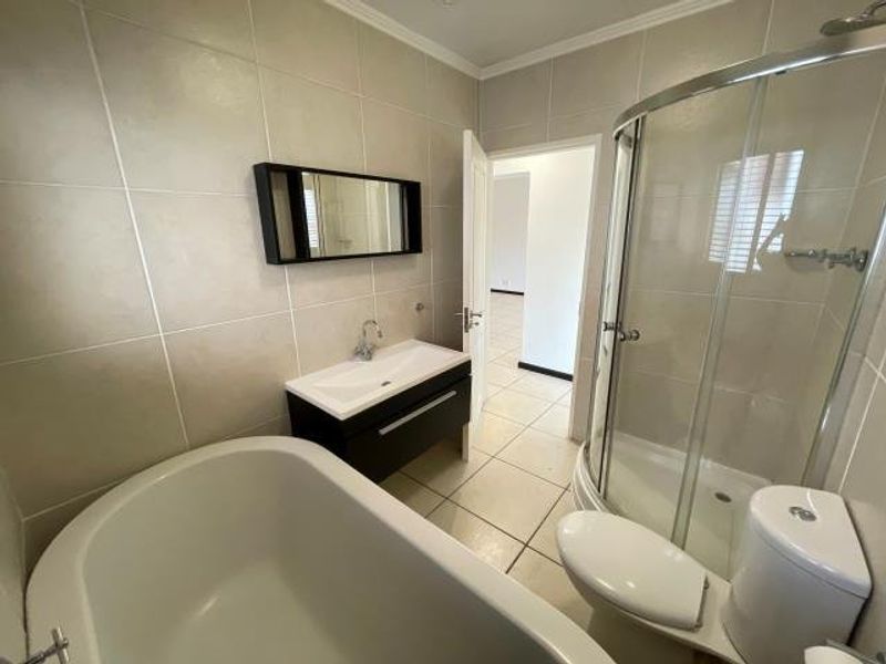 Modern bathroom featuring a freestanding bathtub, corner shower enclosure, vanity cabinet with mirror, and neutral floor and wall tiling.
