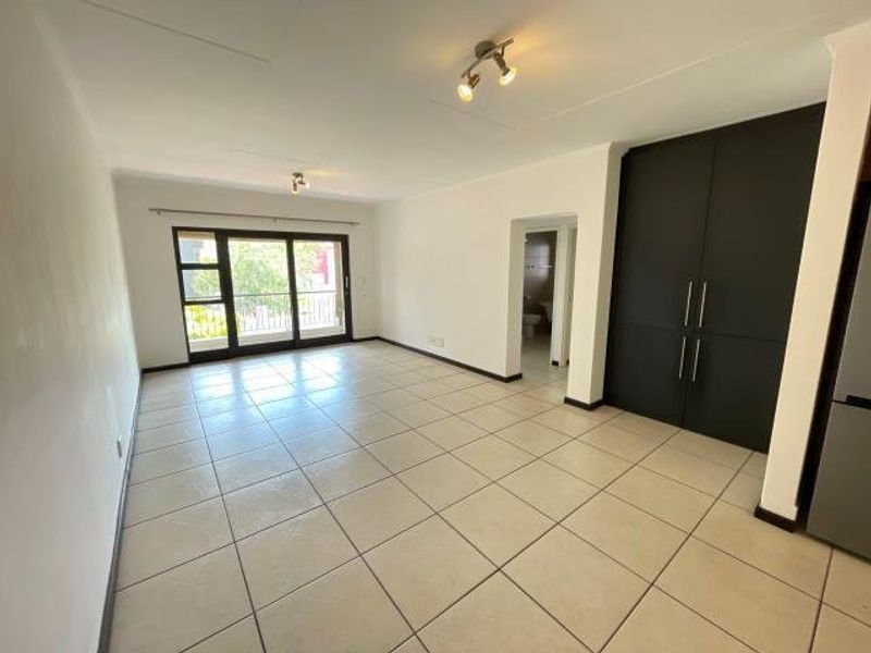 Spacious open-plan living area featuring neutral tiled flooring, modern dark built-in cabinetry, and a large sliding glass door leading to an outdoor balcony.