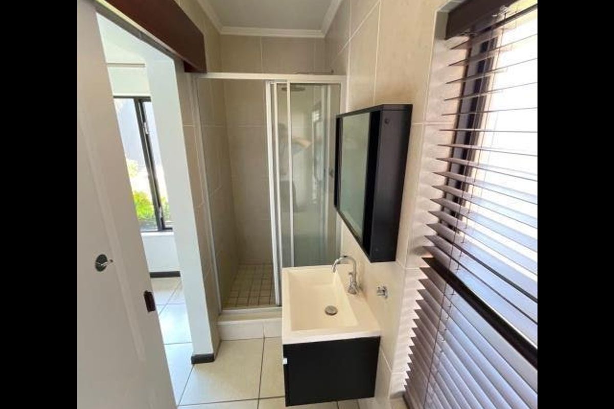 A clean, modern bathroom featuring a glass shower enclosure, wall-mounted vanity with basin, and neutral tiled finishes throughout.