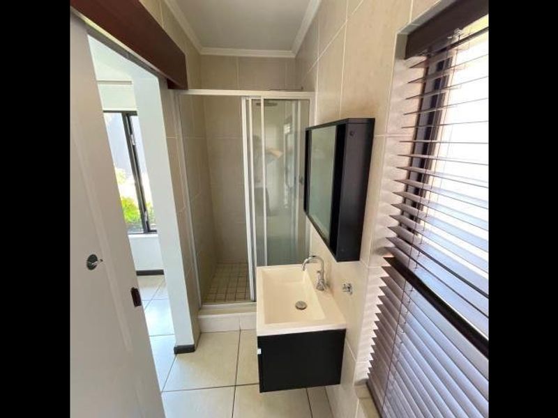 A clean, modern bathroom featuring a glass shower enclosure, wall-mounted vanity with basin, and neutral tiled finishes throughout.