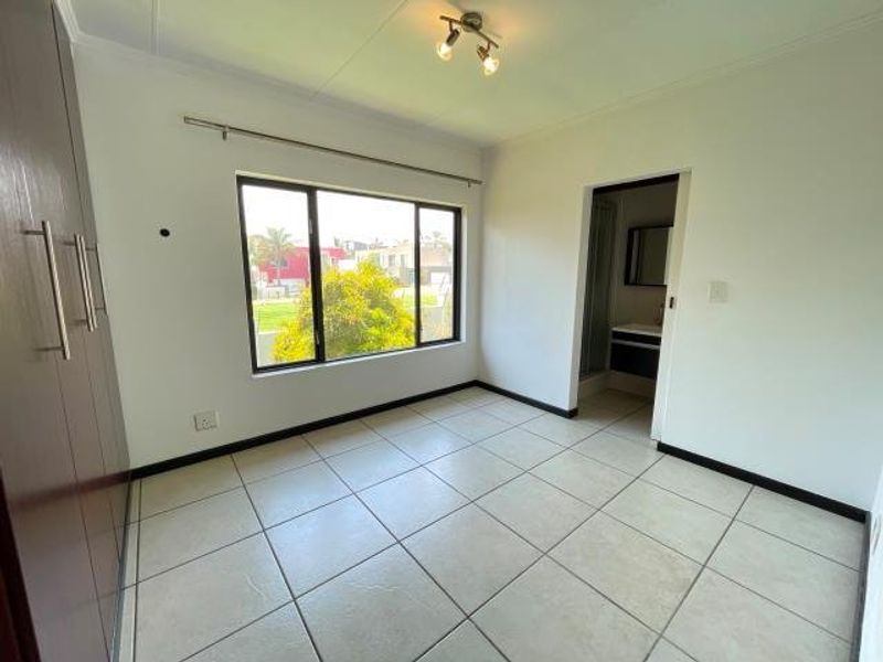 A bright, empty bedroom featuring tiled flooring, built-in cupboards, and an en-suite bathroom, offering a clean and neutral space ready for personalization.