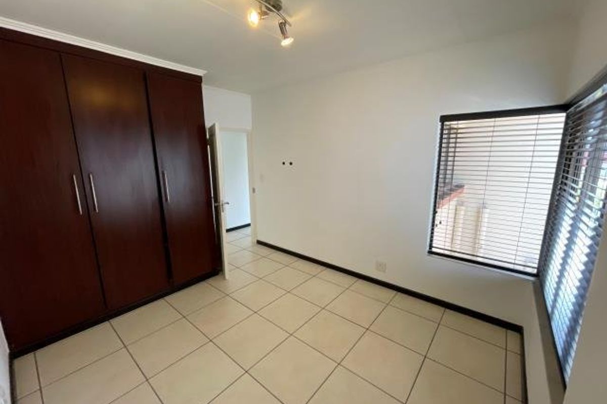 A bright, empty bedroom featuring tiled flooring, built-in wooden cupboards, and venetian blinds on the windows.