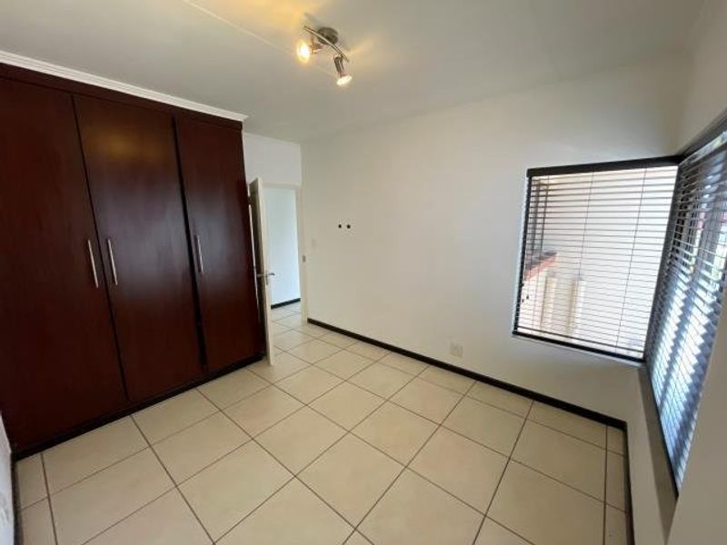 A bright, empty bedroom featuring tiled flooring, built-in wooden cupboards, and venetian blinds on the windows.