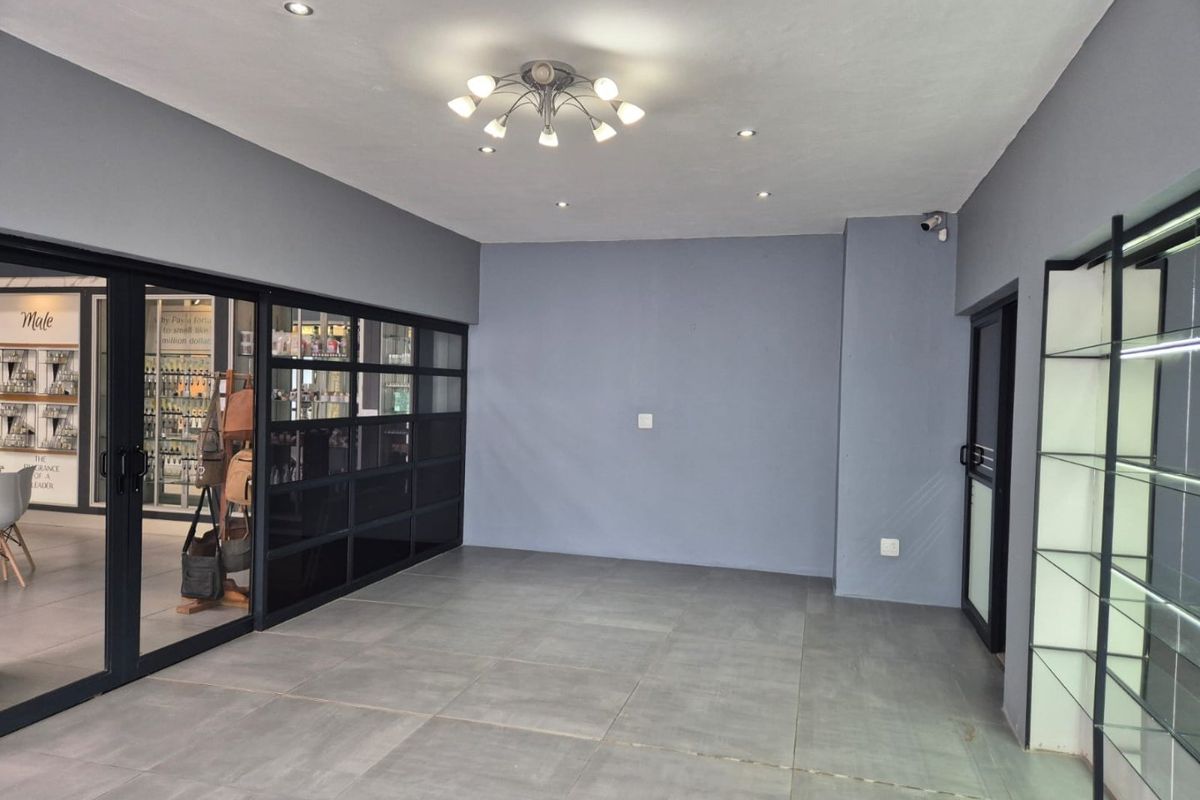 A modern, open-plan commercial space featuring grey tiled flooring, recessed lighting, and a sleek black-framed glass partition, suitable for retail or office use.