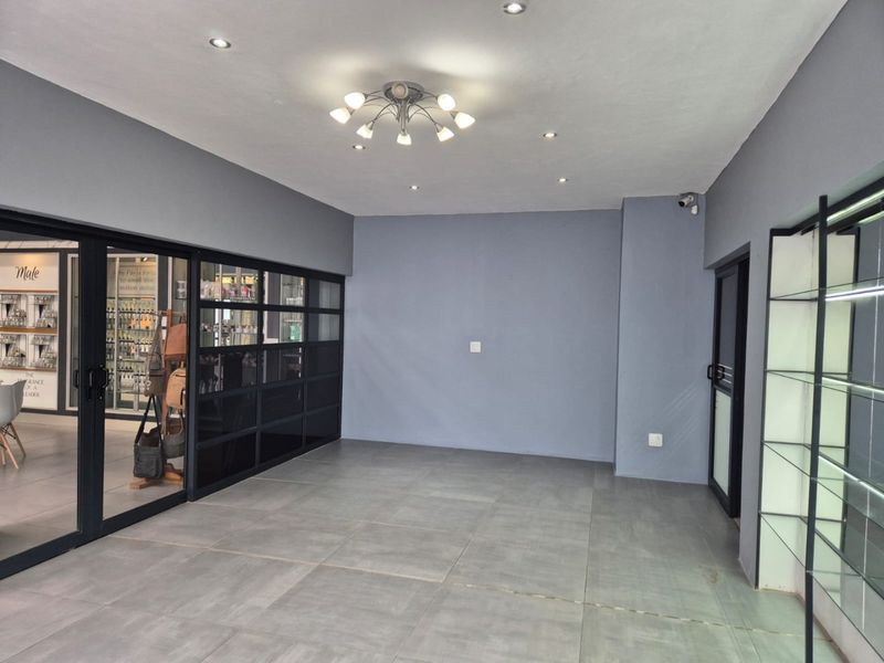 A modern, open-plan commercial space featuring grey tiled flooring, recessed lighting, and a sleek black-framed glass partition, suitable for retail or office use.