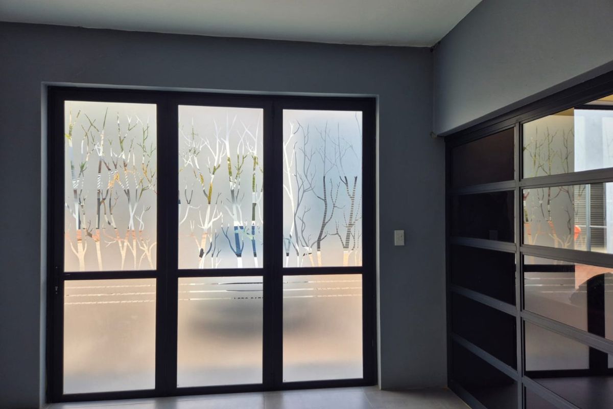 Modern entrance area featuring dark aluminium framed glass doors with decorative frosted film and integrated built-in shelving units.
