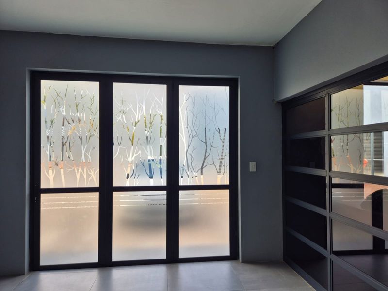 Modern entrance area featuring dark aluminium framed glass doors with decorative frosted film and integrated built-in shelving units.