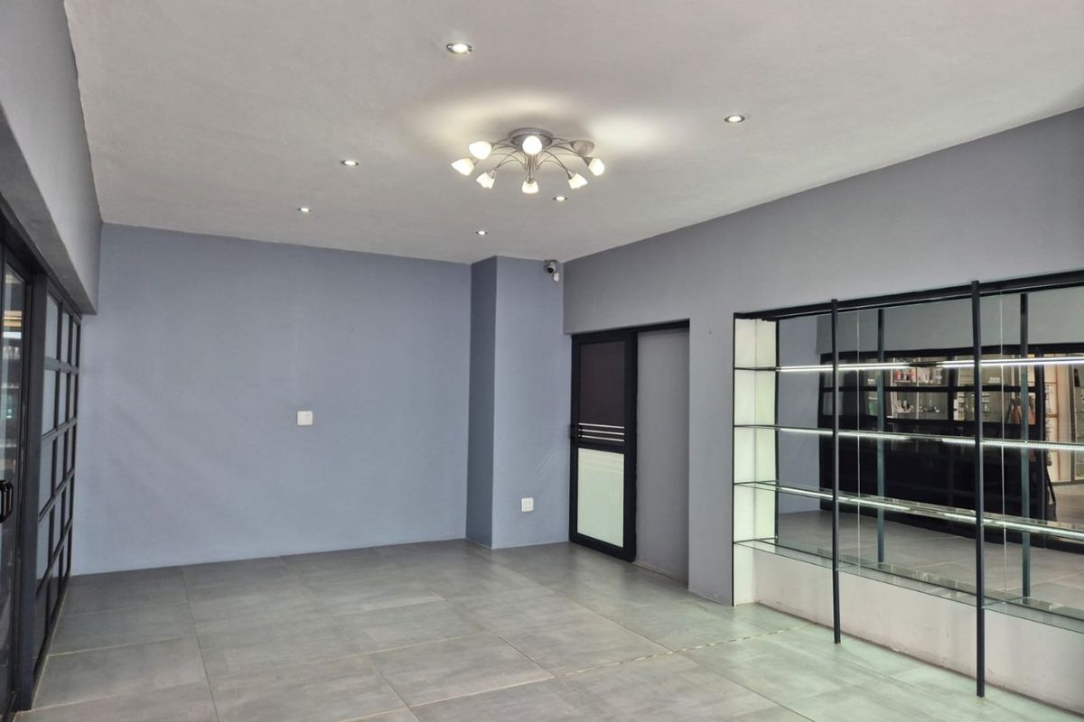 A clean, modern commercial office space featuring large format floor tiles, recessed lighting, and a built-in glass display shelving unit.