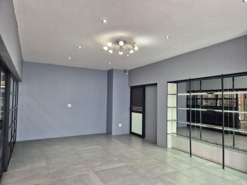 A clean, modern commercial office space featuring large format floor tiles, recessed lighting, and a built-in glass display shelving unit.
