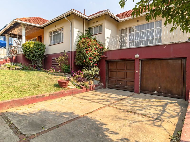 Front elevation of a multi-level house featuring a concrete driveway, double garage, and an upper-level balcony with a tiled roof.