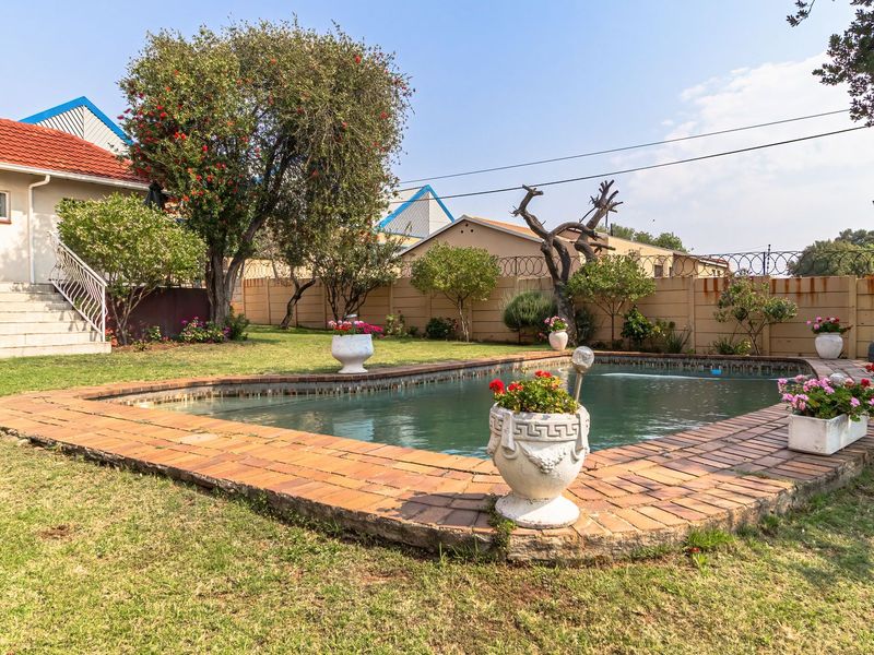 Rear garden featuring a swimming pool with brick coping, surrounded by lawn and a secure boundary wall with an external staircase to the house.