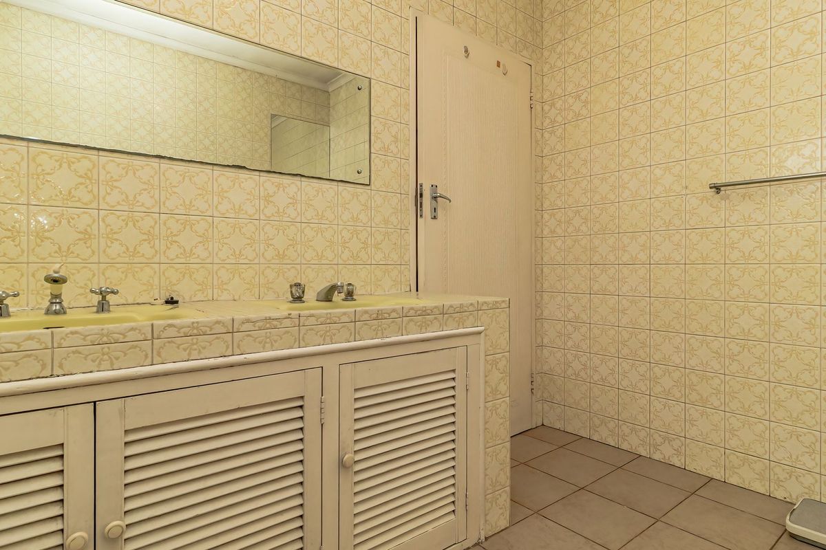 A dated bathroom featuring a tiled vanity with built-in cabinetry, wall-mounted mirror, and full-height wall tiling.