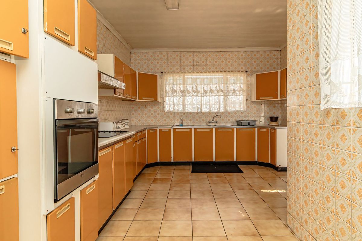A spacious kitchen featuring original dated cabinetry, tiled walls and flooring, and built-in oven, offering significant potential for a modern renovation.
