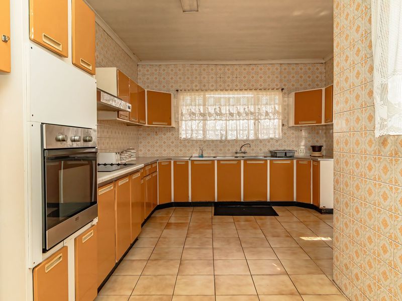 A spacious kitchen featuring original dated cabinetry, tiled walls and flooring, and built-in oven, offering significant potential for a modern renovation.