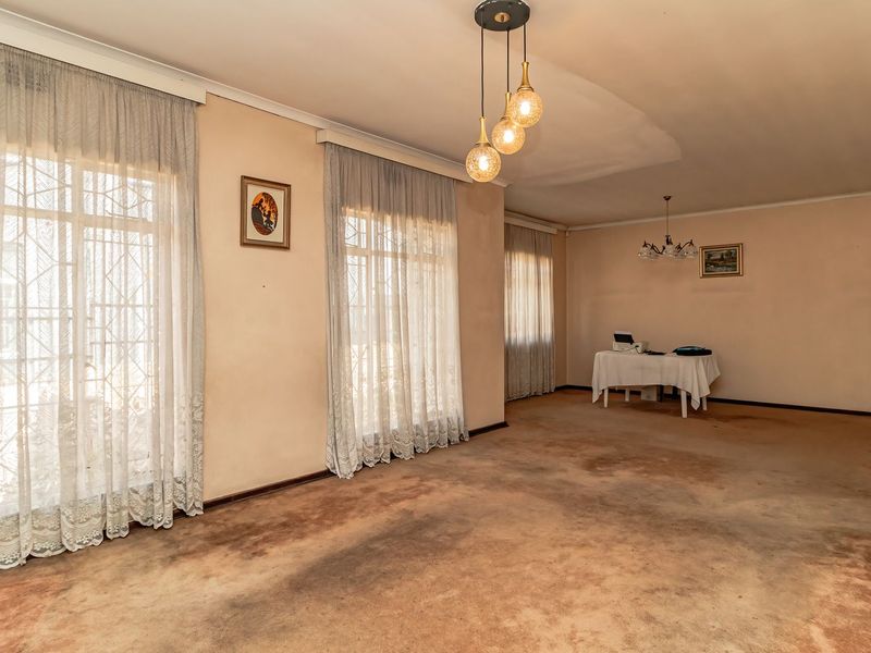 Spacious living area featuring large windows with security gates, pendant lighting, and coved cornicing, requiring significant cosmetic updates and flooring replacement.