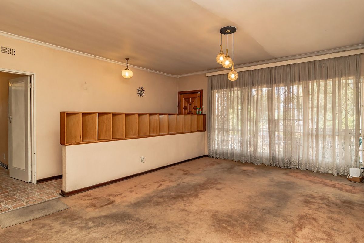 Spacious living room featuring a built-in room divider, pendant lighting, and large windows with curtains. The space requires new flooring and wall finishes.
