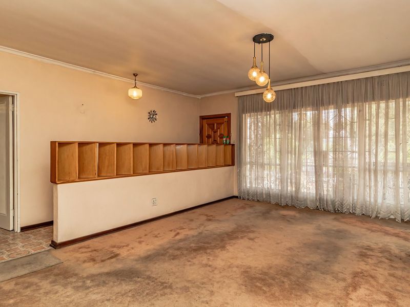 Spacious living room featuring a built-in room divider, pendant lighting, and large windows with curtains. The space requires new flooring and wall finishes.