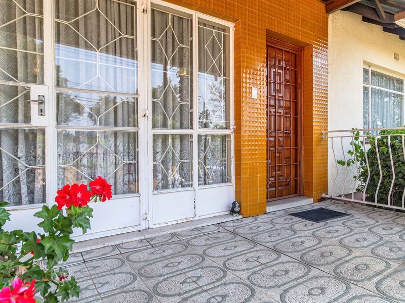 A covered patio area featuring patterned floor tiles, a security gate entrance, and decorative wall tiling, providing a functional outdoor transition space.
