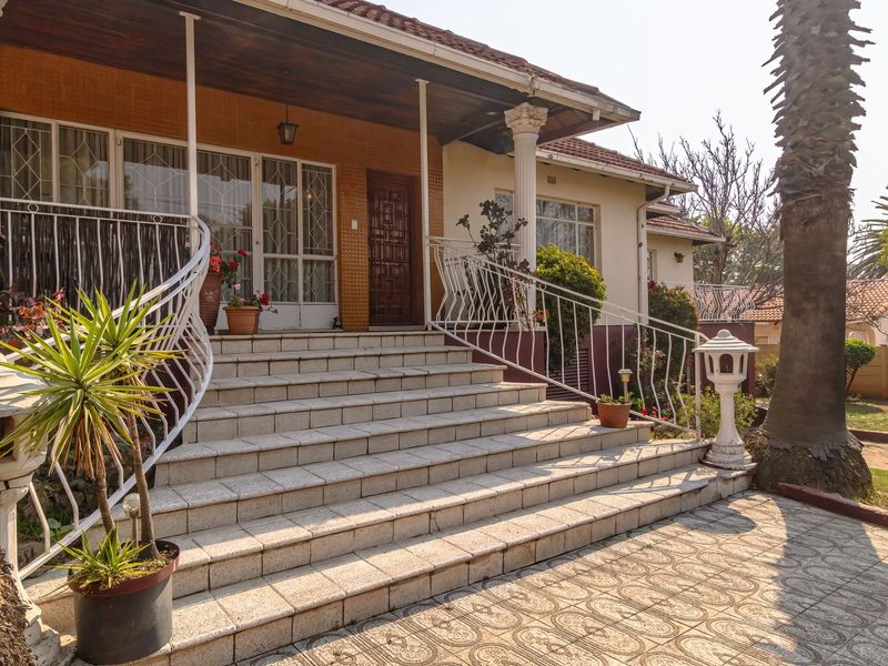 Front entrance of the house featuring a wide tiled staircase, covered veranda, and decorative wrought iron railings leading to the main wooden front door.