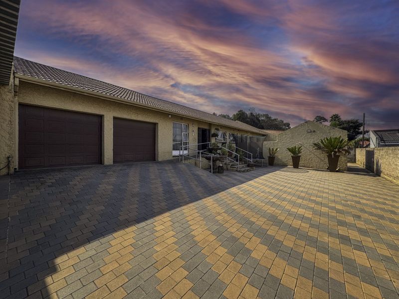 Front exterior view of the property featuring a spacious paved driveway, double garage, and accessible entrance with metal handrails.