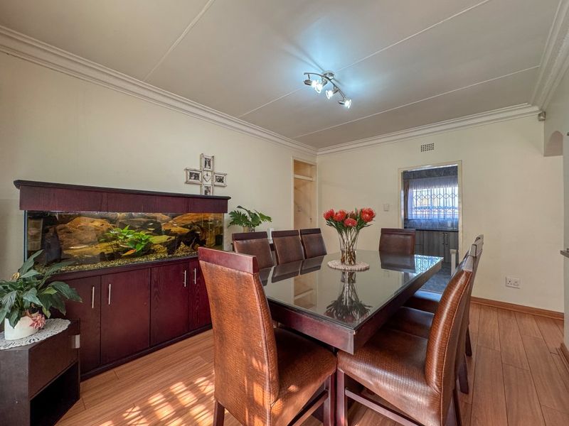 A dining room featuring laminate flooring, coved ceilings, and track lighting, with a view into the adjacent kitchen area.