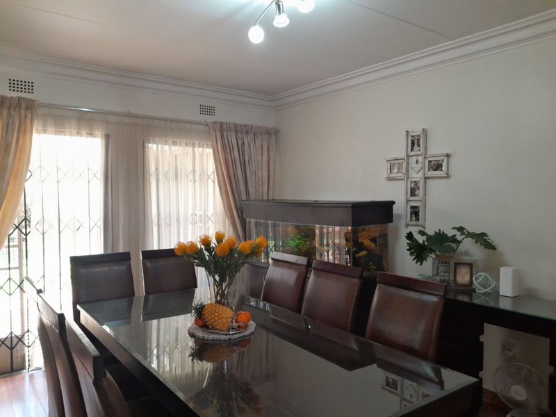 A well-maintained dining room featuring laminate flooring, decorative ceiling cornicing, and large sliding glass doors with security gates providing access to the exterior.