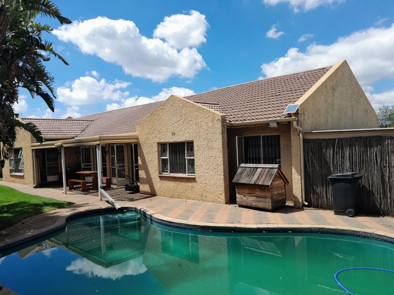 Rear view of the house featuring a swimming pool, paved patio area, and tiled roof structure.