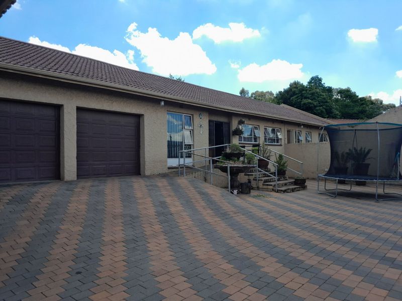 Front exterior view of a single-story house featuring a double garage, paved driveway, and concrete entrance steps with metal handrails.