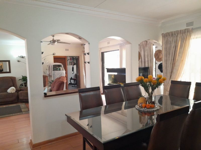 Dining room featuring arched wall openings connecting to adjacent living spaces, laminate flooring, and coved ceiling cornices.