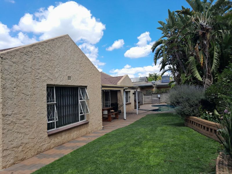 Rear view of the property featuring a paved patio area, a swimming pool, a well-maintained lawn, and established garden landscaping.