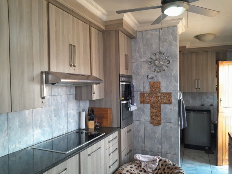 A functional kitchen featuring wood-look cabinetry, granite countertops, built-in oven, electric hob, and a tiled splashback with a ceiling fan.