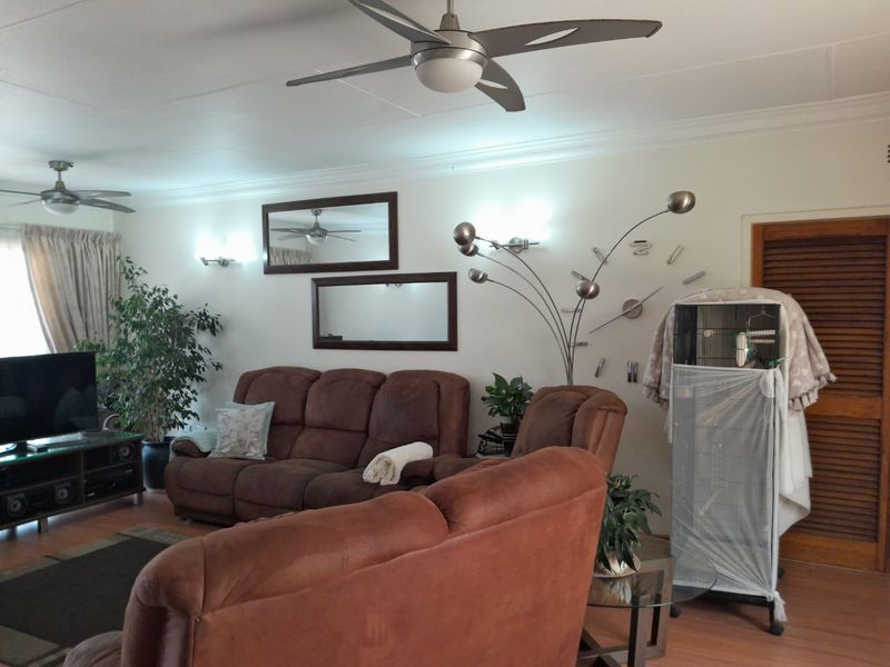 A comfortable living room featuring laminate flooring, ceiling fans, and wall-mounted lighting fixtures, providing a functional and well-lit space.