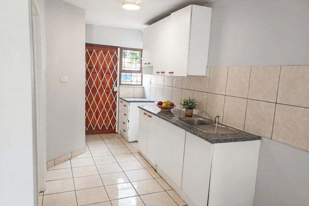 A functional kitchen featuring white cabinetry, granite countertops, a stainless steel sink, tiled backsplash, and tiled flooring with direct access to an exterior door.